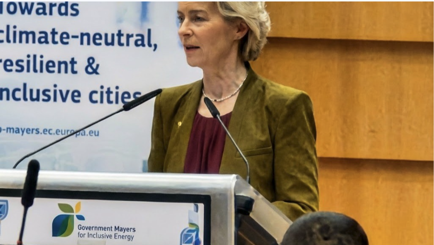 Eine Person an einem Rednerpult vor einem Banner mit der Aufschrift „towards climate-neutral, resilient & inclusive cities“.